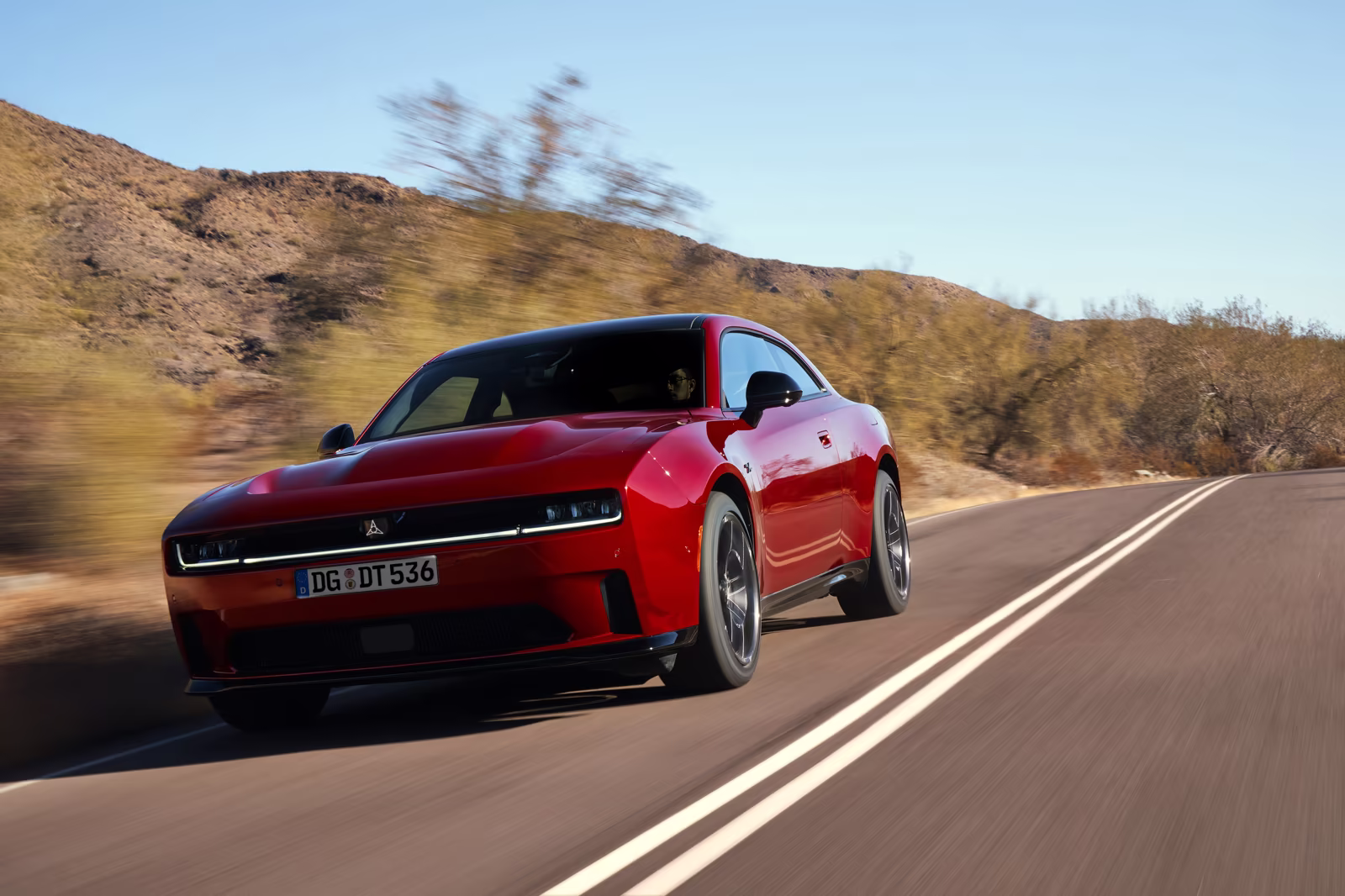 Dodge Charger vermelho em movimento em estrada com montanhas ao fundo