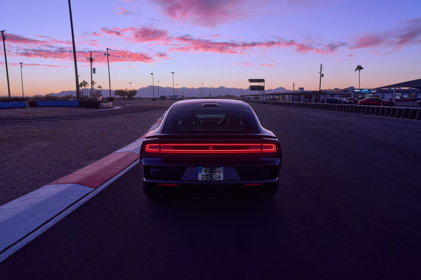 Dodge Charger vermelho visto de traseira em pista ao entardecer