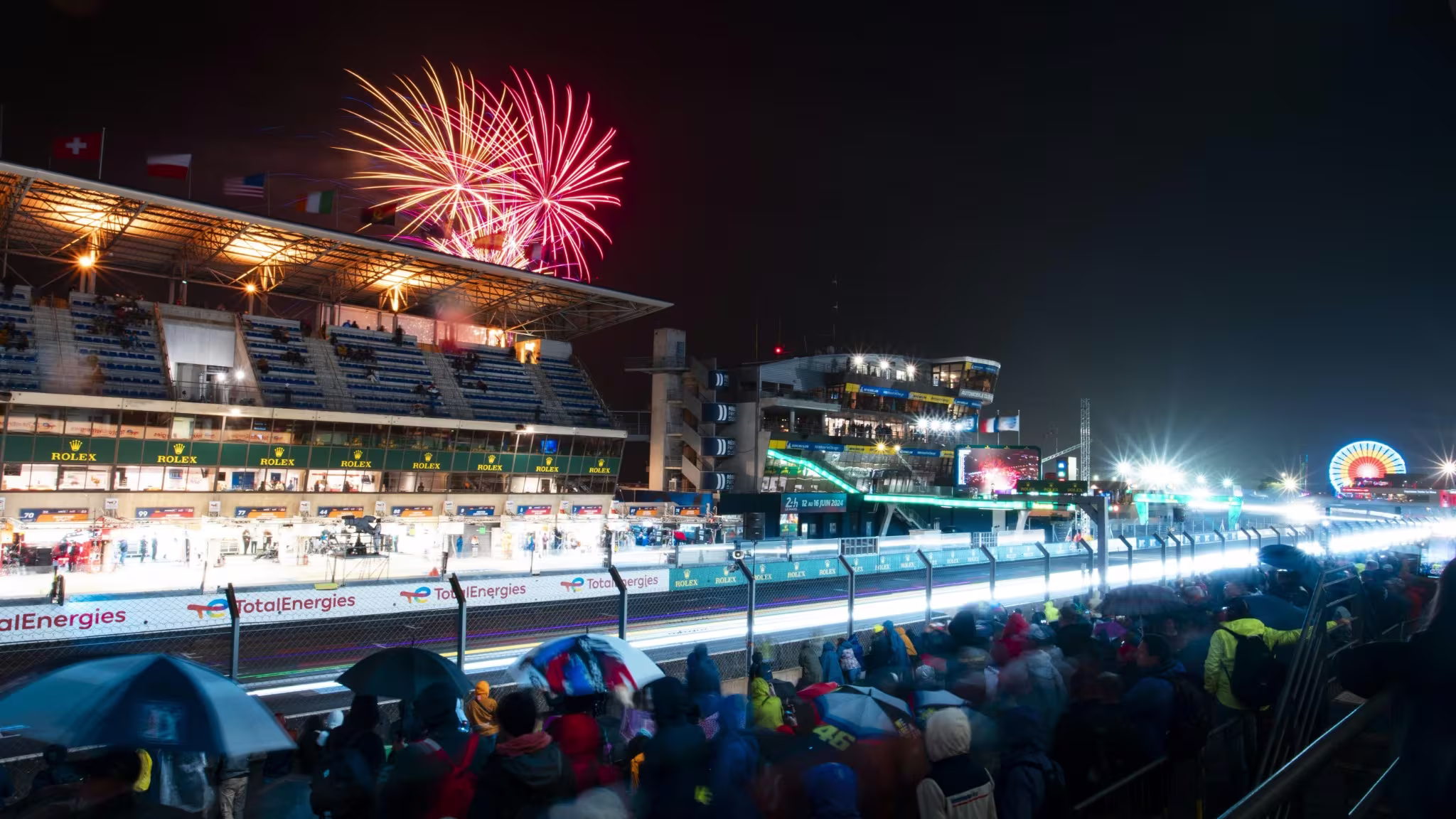 Arquibancada de Le Mans à noite com fogos e carros na pista